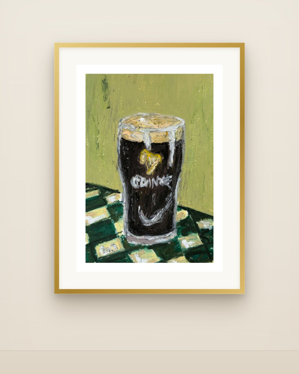 A framed art print featuring a textured painting of a pint of stout with a heart-shaped logo on the glass, set against a green and white checkered tablecloth on a light olive-green background. The print is framed in a gold frame with a white mat, hanging on a beige wall.